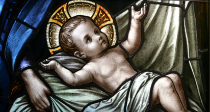 Na zdjęciu jest witraż przedstawiający Dzieciątko Jezus leżące na sianie, w pozłacanej aureoli, z uniesioną prawą ręką. Tło jest niebieskie, a witraż zdobi kartka świąteczna z życzeniami.