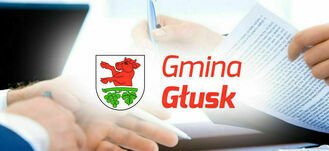 Zdjęcie przedstawia osobę podpisującą dokument przy biurku z laptopem, na pierwszym planie logo z napisem "Gmina Głusk" z czerwonym bykiem.