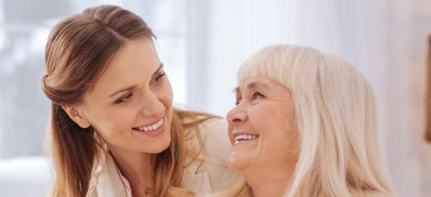 Dwie uśmiechnięte kobiety, młodsza z ramieniem wokół starszej, siedzą w jasnym pomieszczeniu. Na dole strony znajdują się informacje o bezpłatnych badaniach mammograficznych.