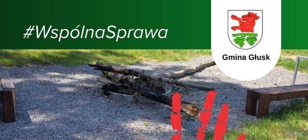 Na zdjęciu znajduje się plakietka z hasztagiem "#WspólnaSprawa" oraz napisem "STOP! Aktom wandalizmu". W tle widać zniszczoną ławkę w otoczeniu trawy i kamieni oraz herb Gminy Głusk.