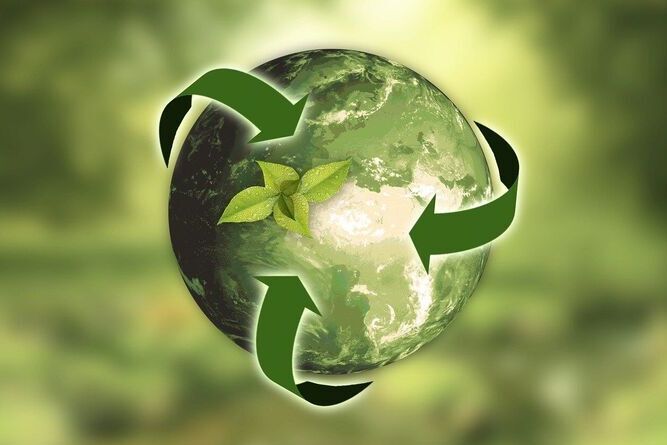 Grafika przedstawiająca ziemię z umieszczonymi na niej zielonymi liśćmi i otaczającymi ją zielonymi strzałkami symbolizującymi recykling, na rozmytym tle w kolorach zieleni.