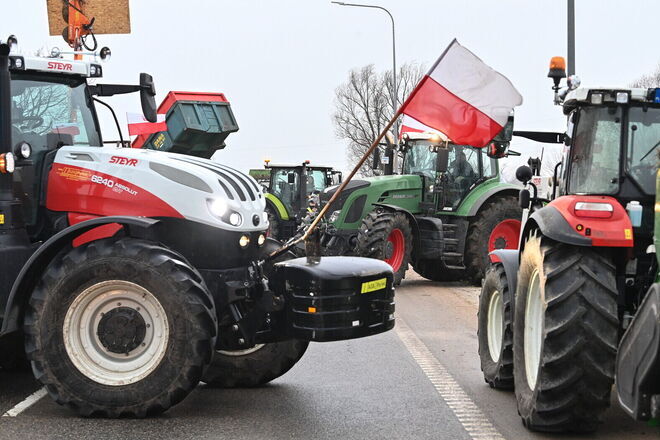 Zdjęcie przedstawia protest rolników z użyciem ciągników. Widoczny ciągnik marki Steyr z polską flagą, w tle kolejne traktory.
