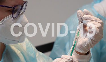 Na zdjęciu napis COVID-19 na tle osoby ze strzykawką