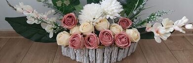 Kompozycja kwiatowa w drewnianym pojemniku, z różowymi i kremowymi różami oraz białymi kwiatami i zielenią.