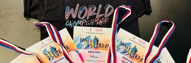 Na zdjęciu czarna koszulka z napisem "World Championship" oraz zestaw pięciu dyplomów i medali z zawodów tanecznych w Ostrawie, w tym nagrody za pierwsze i drugie miejsca.