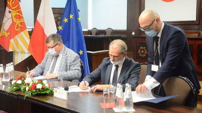 trzech mężczyzn przy stole podpisujący dokumenty