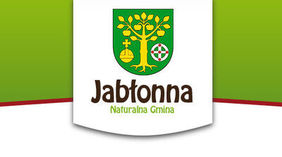 Herb Jabłonny przedstawia złote drzewo z owocami na zielonym tle, pod nim jabłko oraz tarczę. Poniżej napis "Jabłonna Naturalna Gmina" w brązowo-zielonej kolorystyce.