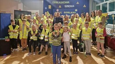 zdjęcie grupy dzieci i policjanta, ubranych w odblaskowe kamizelki