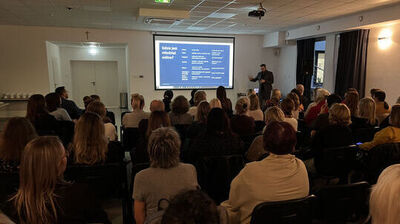 zdjęcie siedzącej tyłem grupy osób i prowadzącego szkolenie