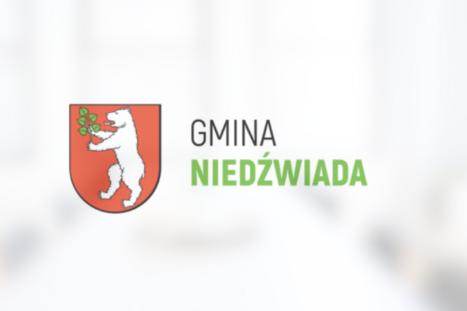 Herb Gminy Niedźwiada przedstawiający białego niedźwiedzia trzymającego zieloną gałązkę na czerwonym tle, powyżej napis "GMINA NIEDŹWIADA".