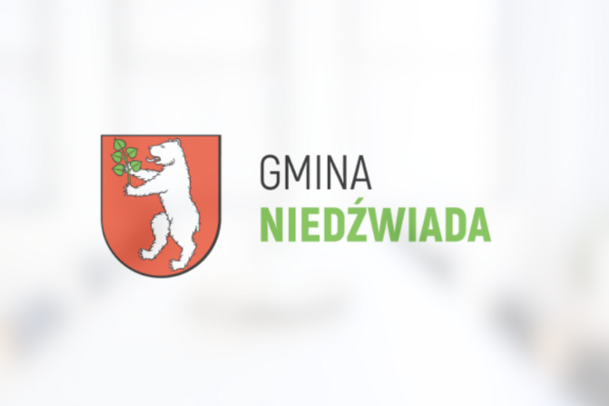 Herb Gminy Niedźwiada przedstawiający białego niedźwiedzia trzymającego zieloną gałązkę na czerwonym tle, powyżej napis "GMINA NIEDŹWIADA".