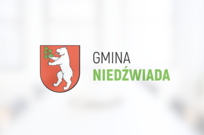 Herb Gminy Niedźwiada przedstawiający białego niedźwiedzia trzymającego zieloną gałązkę na czerwonym tle, powyżej napis "GMINA NIEDŹWIADA".