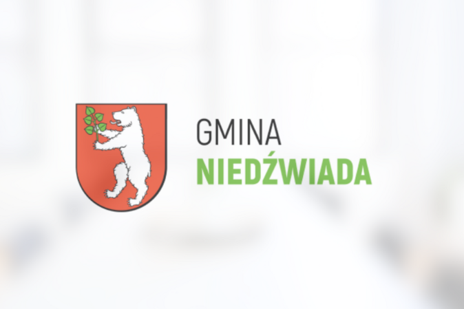 Herb Gminy Niedźwiada przedstawiający białego niedźwiedzia trzymającego zieloną gałązkę na czerwonym tle, powyżej napis "GMINA NIEDŹWIADA".