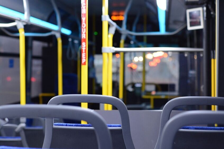 Wnętrze autobusu nocą z widokiem na niebieskie siedzenia, żółte poręcze i ostrzeżenie "Watch your step" na wyświetlaczu.