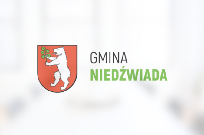 Herb Gminy Niedźwiada przedstawiający białego niedźwiedzia trzymającego zieloną gałązkę na czerwonym tle, powyżej napis "GMINA NIEDŹWIADA".