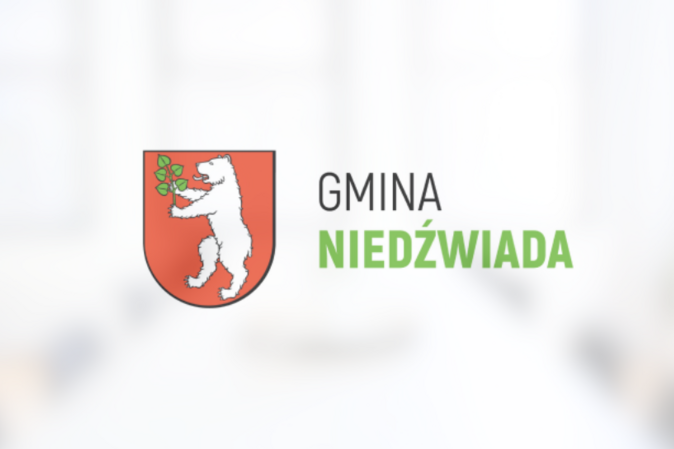 Herb Gminy Niedźwiada przedstawiający białego niedźwiedzia trzymającego zieloną gałązkę na czerwonym tle, powyżej napis "GMINA NIEDŹWIADA".