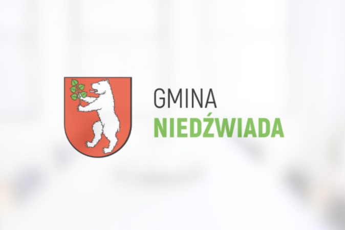 Herb Gminy Niedźwiada przedstawiający białego niedźwiedzia trzymającego zieloną gałązkę na czerwonym tle, powyżej napis "GMINA NIEDŹWIADA".