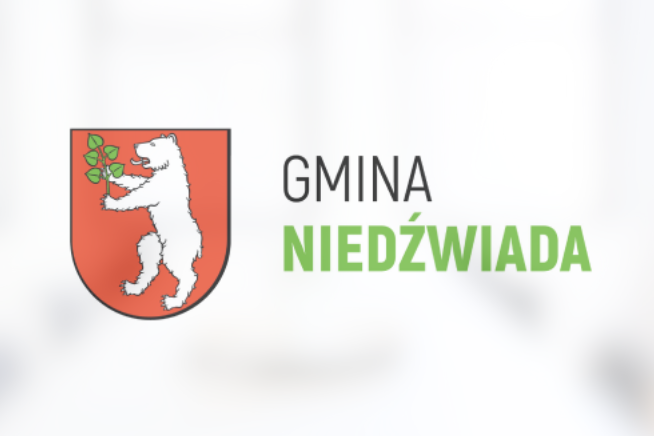 Herb Gminy Niedźwiada przedstawiający białego niedźwiedzia trzymającego zieloną gałązkę na czerwonym tle, powyżej napis "GMINA NIEDŹWIADA".