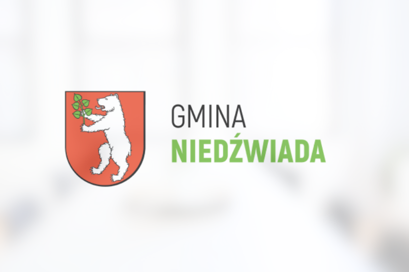 Herb Gminy Niedźwiada przedstawiający białego niedźwiedzia trzymającego zieloną gałązkę na czerwonym tle, powyżej napis "GMINA NIEDŹWIADA".