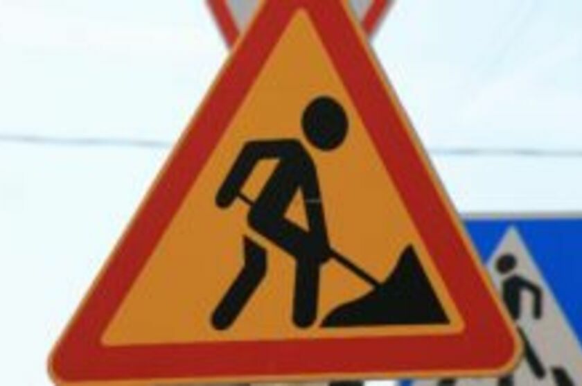 Znak ostrzegawczy z symbolem pracownika drogowego z łopatą obok stosu ziemi, oznaczający teren robót drogowych.