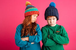 Zdjęcie przedstawia rudowłosą dziewczynkę oraz chłopca w czapkach na różowym tle 