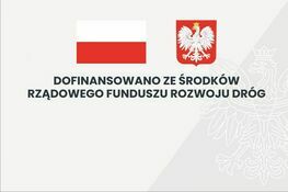 Zdjęcie przedstawia grafikę z polską flagą i godłem Polski po prawej stronie. Po lewej napis: "Dofinansowano ze środków Rządowego Funduszu Rozwoju Dróg".