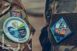 Zdjęcie zbliżenia munduru wojskowego z naszywkami: flagą Wielkiej Brytanii, emblematem NATO i znaczkiem ćwiczeń "Dragon 24" oraz "Defender Europe".