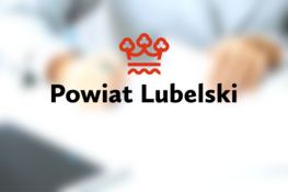 Logo Powiatu Lubelskiego na rozmytym tle z ludźmi w biurze; czerwona korona i napis na jasnym tle.