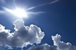 Słoneczne niebo z kilkoma puszystymi chmurami; promienie słoneczne przedzierają się przez błękitną przestrzeń.