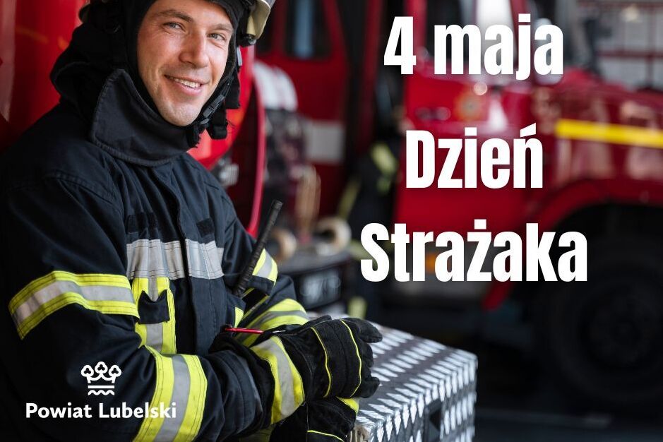 Strażak w hełmie i mundurze uśmiecha się, stojąc przed wozem strażackim. Obok niego napis: "4 maja Dzień Strażaka". Na dole logo Powiatu Lubelskiego.