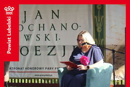 Starosta Lubelski - dr inż. Sylwia Pisarek Piotrowska siedzi na scenie, czytając książkę. Za nią transparent z napisem "Jan Kochanowski Poezja". Wydarzenie to Narodowe Czytanie 2025 w Zespole Szkół im. A. Kwiatkowskiego w Bychawie.