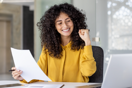 Kobieta z kręconymi włosami siedzi przy biurku, trzyma dokumenty i unosi zaciśniętą pięść w geście sukcesu. Po lewej stronie tekst: „Program NaszEauto. Jak złożyć dobry wniosek?” oraz logotypy partnerów projektu.