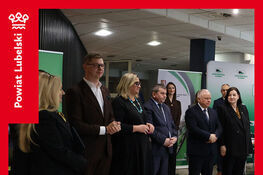 Grupa osób w eleganckich strojach stoi w rzędzie w budynku. Za nimi są zielone banery. W rogu plakatu widnieje napis "Dzień Kariery 2026 na Uniwersytecie Przyrodniczym w Lublinie".