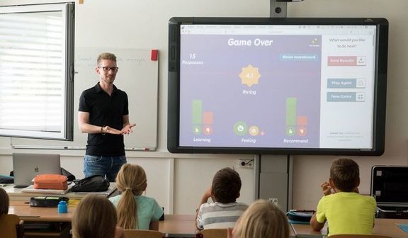 Klasa z uczniami i nauczycielem stojącym przy interaktywnej tablicy. 