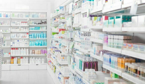 Wnętrze apteki z półkami wypełnionymi różnorodnymi opakowaniami produktów leczniczych i pielęgnacyjnych, z naciskiem na niebieskie i białe barwy.