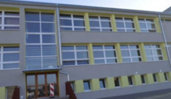 Zdjęcie 1: Trzypiętrowy budynek edukacyjny z szeregiem niebieskich okien i drzewem z przodu.

Zdjęcie 2: Odnowiony trzypiętrowy budynek szkoły z żółtymi i niebieskimi detalami, wejście z czerwonymi schodami.