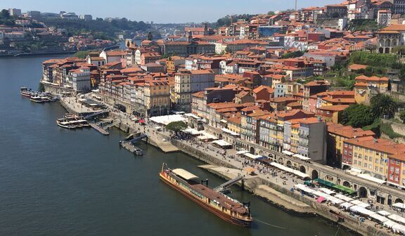 Widok na rzekę Douro w Porto, z barwnymi budynkami na brzegu i łodziami na wodzie, w tle pagórkowate miasto pod błękitnym niebem.