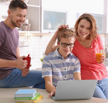 Rodzina spędza czas razem w jasnym wnętrzu: uśmiechnięci rodzice oglądają laptop z synem, który ma na sobie okulary. Na stole kubki i książki.