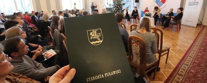 Powiatowe święto wolontariatu - sala Pompejańska w tle. Na pierwszym miejscu herb powiatu z napisem starosta puławski.