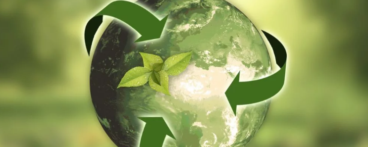 Stylizowana planeta Ziemia z zielonymi strzałkami w kształcie symbolu recyklingu wokół niej. Na środku planety znajduje się zielony liść. Tło jest rozmyte i ma zielono-brązowe odcienie.