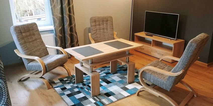 Na zdjęciu pokój, stół trzy fotele i telewizor