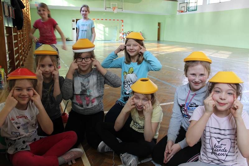 Zdjęcie dzieci na sali gimnastycznej na głowach mają żółte plastikowe czapeczki