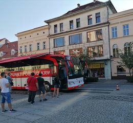 Zdjęcie przedstawia ludzi stojących przed krwiobusem w rynku