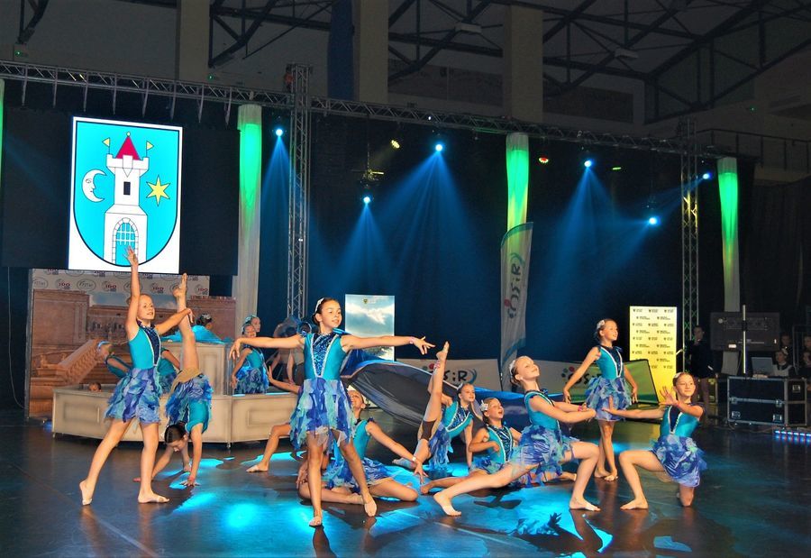 Na zdjęciu widać tancerki w niebieskich strojach, tańczące na scenie, a nad nimi widać herb Świebodzic 