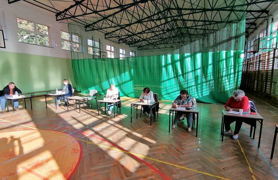 Zdjęcie przedstawia reprezentantów organizacji pozarządowych podczas głosowania. Na zdjęciu widać cztery kobiety siedzące w sali gimnastycznej przy ławkach. Z tyłu widoczna jest zielona zasłona.