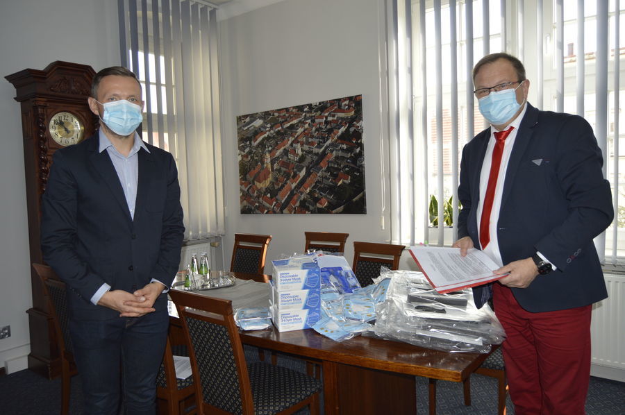 Na zdjęciu: Aleksander Maicher i burmistrz miasta Paweł Ozga stoją przodem. Na stole leżą przekazane środki ochrony osobistej.