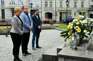 Na zdjęciu widoczne są trzy osoby stojące przed pomnikiem Papieża: sekretarz miasta, burmistrza miasta, zastępcę burmistrza miasta.