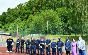 Poziomy prostokąt na zdjęciu widoczne osoby stojące w rzędzie na boisku szkolnym.