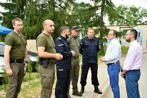 Na zdjęciu widać siedmiu mężczyzn stojących w na drodze, w tle widać drzewa.