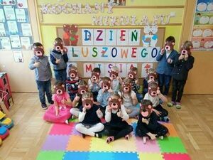 Na zdjęciu widnieje grupa przedszkolaków na tle ścianki z napisem dzień pluszowego misia.